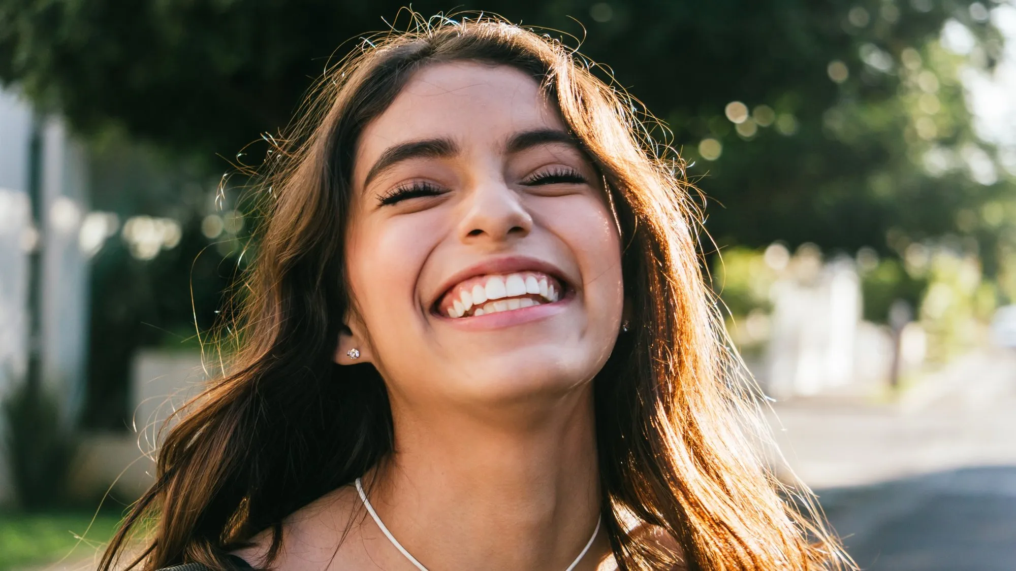 A woman laughing outdoors in warm evening light.